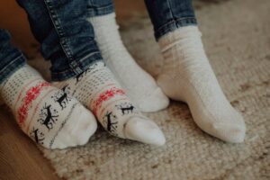 Two people wearing festive socks on a cozy carpet floor indoors.