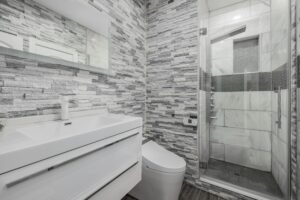 Stylish modern bathroom featuring a glass shower, stone walls, and sleek white vanity.