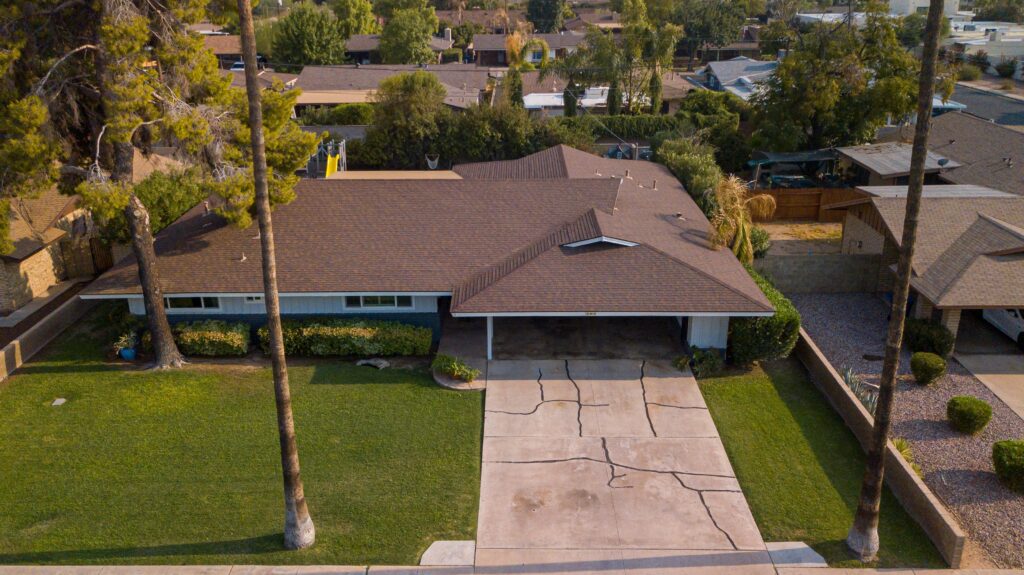 Drone shot of a suburban house and driveway surrounded by greenery in a quiet neighborhood.