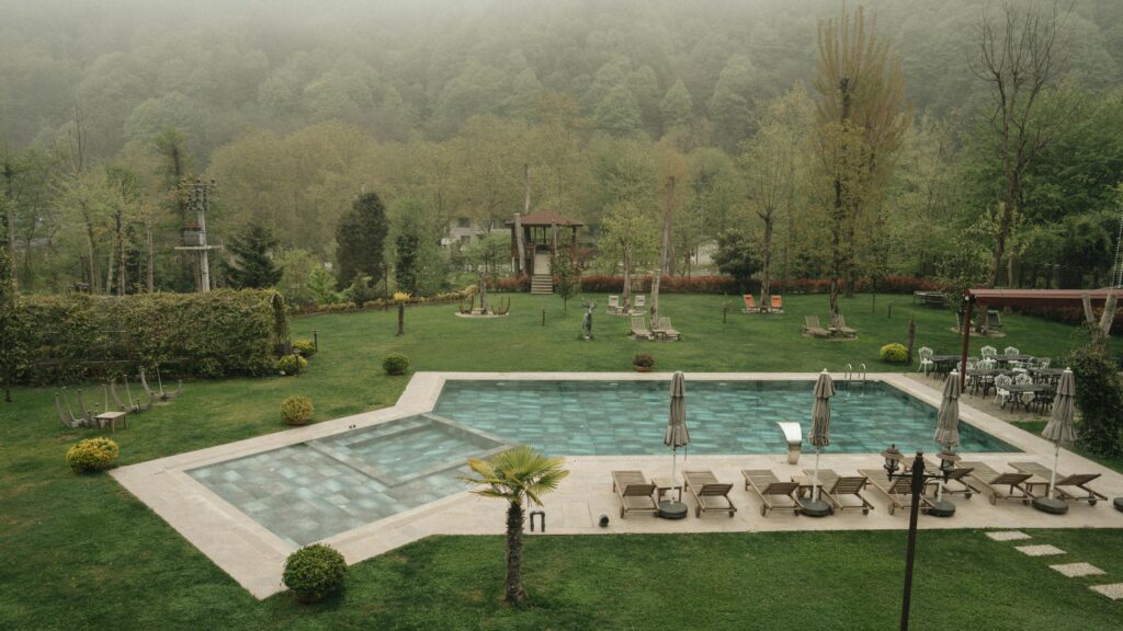 A peaceful outdoor pool surrounded by lush greenery and misty woods, perfect for relaxation.