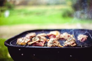 Juicy meat sizzling on a grill outdoors, seasoned with fresh rosemary for a mouthwatering meal.
