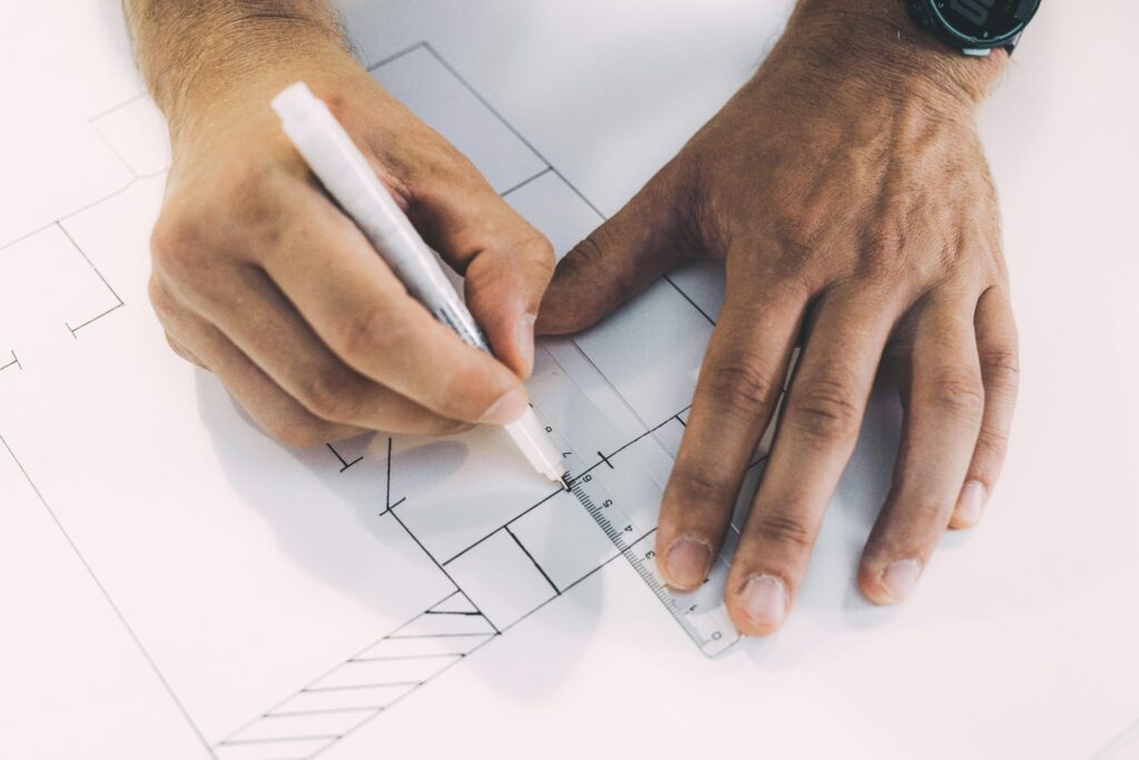 Hands sketching architectural plans with precision using ruler and pen on paper.