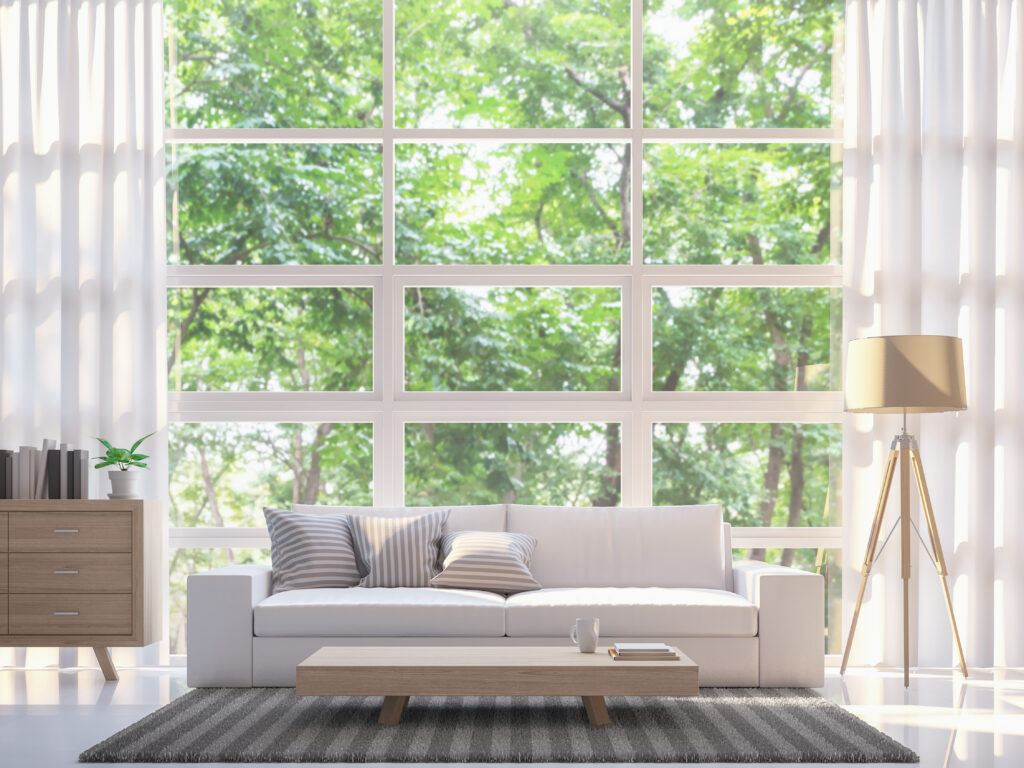 A sunlit living room showing a low-profile sofa placed carefully in front of a large window with sheer curtains.