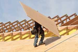 A construction worker installing sturdy plywood roof decking sheets on a residential house frame.