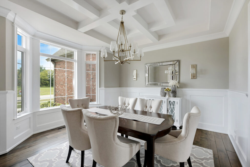 A formal dining room featuring a coffered ceiling, bold navy blue wallpaper, and a large round wooden table with upholstered chairs.
