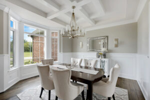 A formal dining room featuring a coffered ceiling, bold navy blue wallpaper, and a large round wooden table with upholstered chairs.