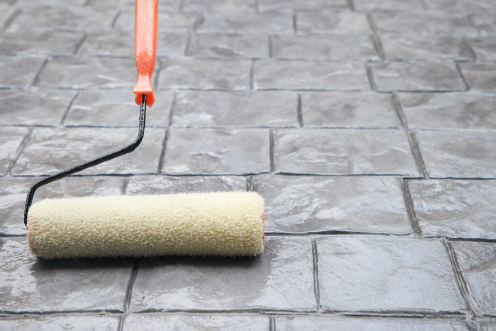 Worker applying penetrating concrete sealer with roller on outdoor patio
