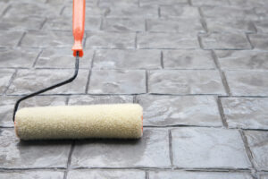 Worker applying penetrating concrete sealer with roller on outdoor patio
