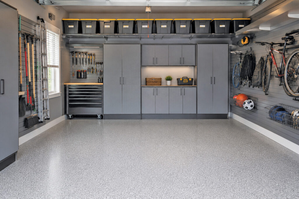 Organized garage with gray storage cabinets, slatwall tool and bike storage, and a gray epoxy speckled floor