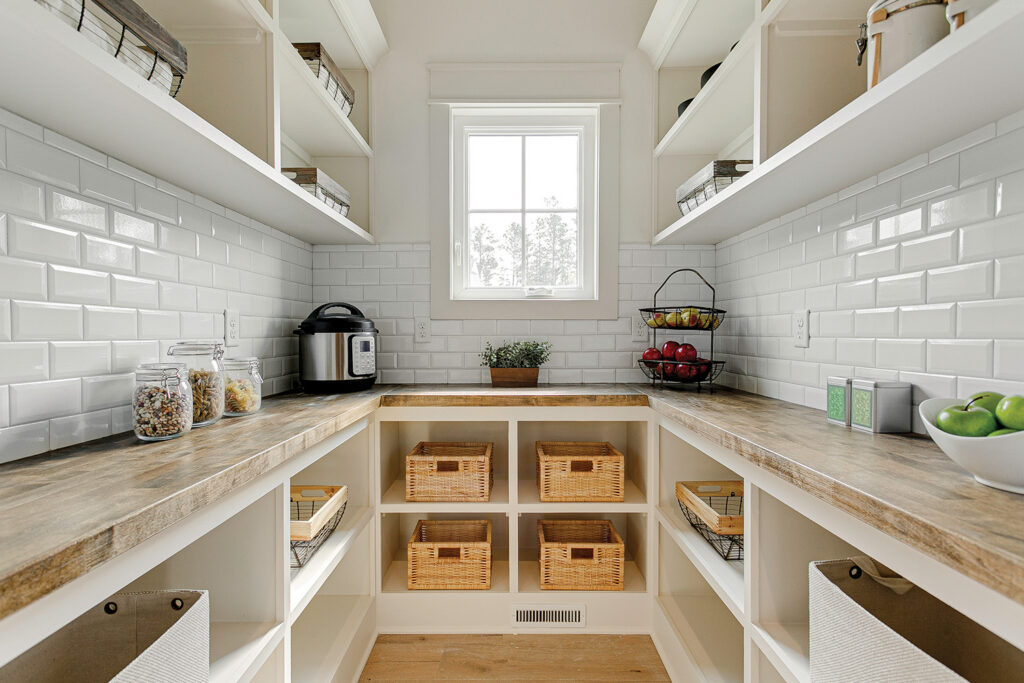 Organized walk-in pantry with white subway tile, open shelving, woven storage baskets and butcher block counters