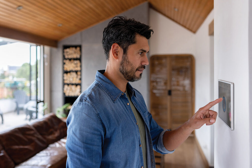 Man using a wall-mounted smart home control panel in a modern living room with wood ceiling