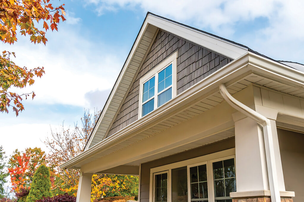 Home roofline, gutters and gable with fall foliage nearby against a blue sky in early autumn