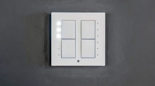 A modern interior wall featuring a sleek, minimalist smart light switch with a glowing LED indicator