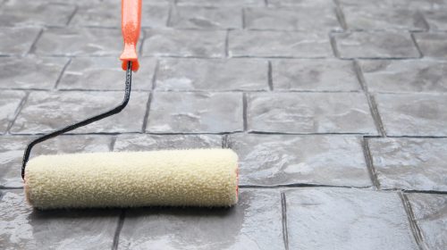 Worker applying penetrating concrete sealer with roller on outdoor patio
