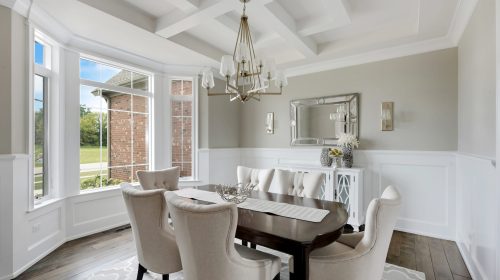 A formal dining room featuring a coffered ceiling, bold navy blue wallpaper, and a large round wooden table with upholstered chairs.