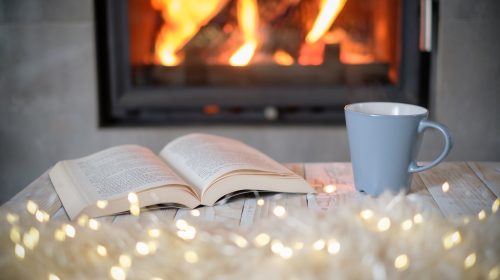 Open book and cup of tea near burning fireplace. Hygge concept