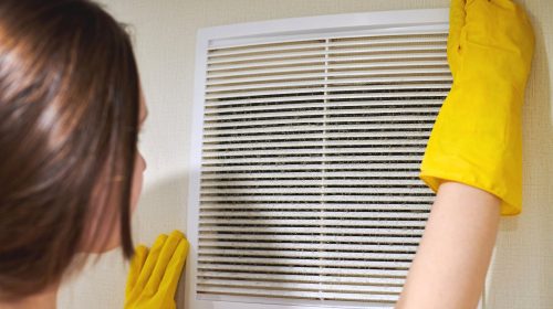 Hands in protective rubber gloves opening clogged air ventilation grill of HVAC with dusty filter to clean or replace it. Cleaning service concept.