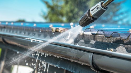 Spring Rain Gutters Cleaning Using Pressure Washer. Closeup Photo.
