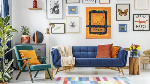 Green armchair next to blue settee in colorful living room interior with painting and posters. Real photo