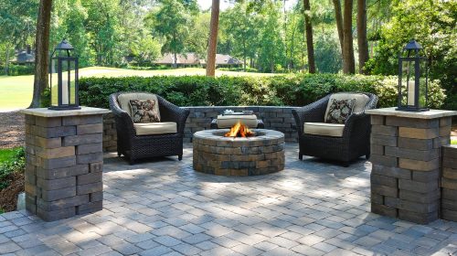 A beautiful outdoors pavers with two comfortable armchairs and a fire pit in a natural green environment