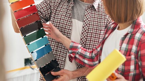 Bearded man holding a colored medium-density fiberboard sample kit in front of a female painter