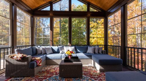 Cozy screened porch with contemporary furniture and flower bouquet in a vase, autumn leaves and woods in the background.