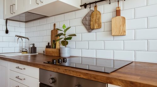 Kitchen brass utensils, chef accessories. Hanging kitchen with white tiles wall and wood tabletop.Green plant on kitchen background side view