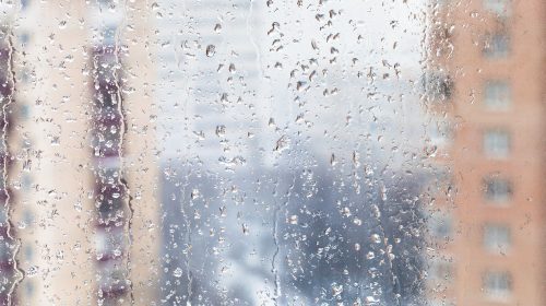 urban background - rain drops on home window glass (focus on water trickles on windowpane) in winter season