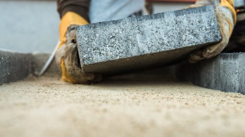 Builder laying a paving brick placing it on the sand foundation with gloved hands.