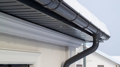 Corner of the house with new gray metal tile roof and rain gutter at winter. Metallic Guttering System, Guttering and Drainage Pipe Exterior