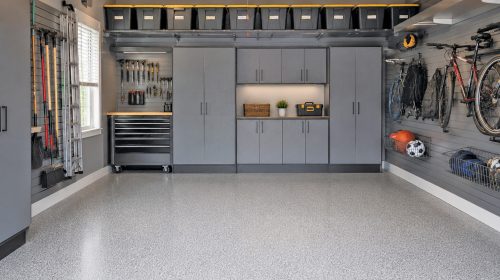 Organized garage with gray storage cabinets, slatwall tool and bike storage, and a gray epoxy speckled floor