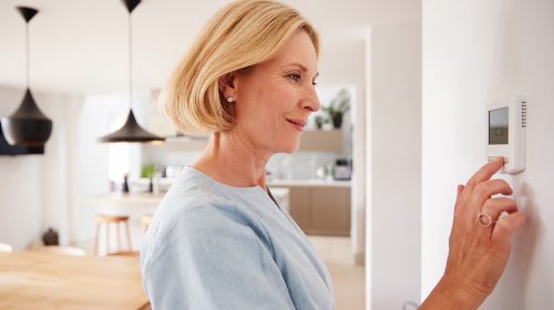 Woman adjusting a wall-mounted thermostat in a bright modern kitchen and dining area