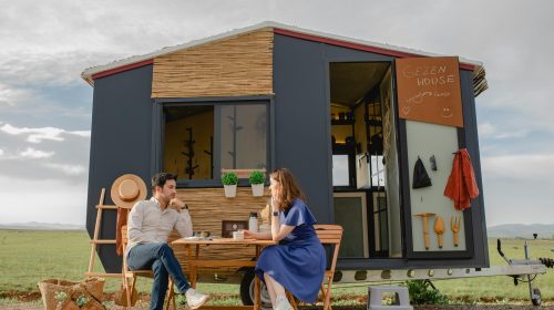 A young couple relaxing at a picnic table outside a modern tiny home in nature.