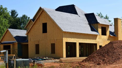 A partially built wooden house under construction, showcasing its progress and design in daylight.