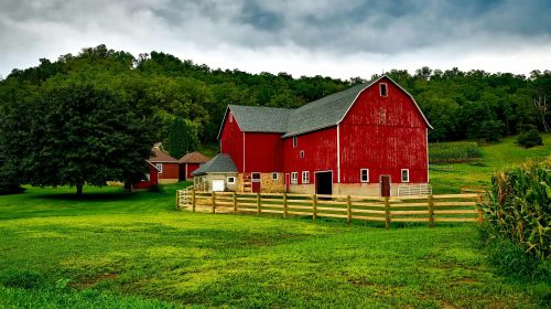 Vibrant red barn amidst lush greenery and cloudy skies in Wisconsin.
