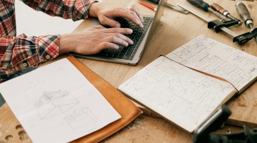 A woodworker uses a laptop to design furniture in a workshop setting, highlighting the blend of technology and craftsmanship.