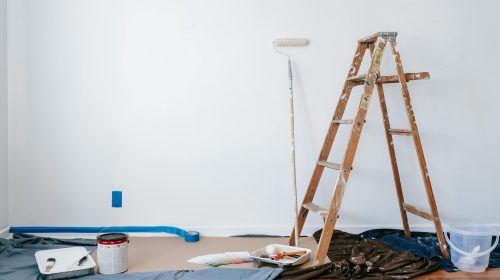 A room prepared for renovation with a ladder, paint supplies, and drop cloth.